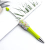 A bright lime green ballpoint pen with a sparkly, iridescent sequin top resting on white paper.