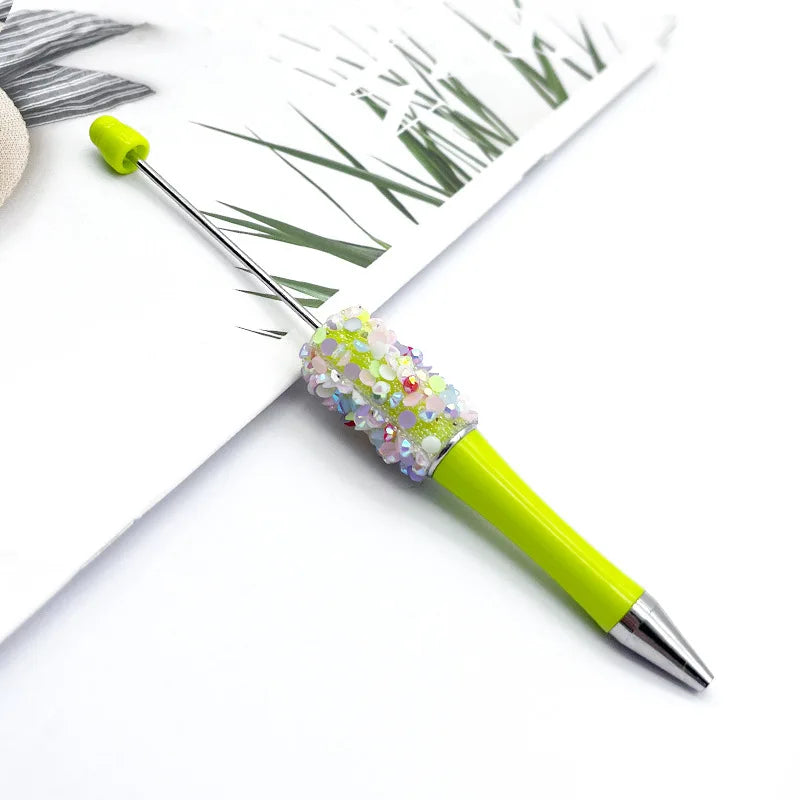 A bright lime green ballpoint pen with a sparkly, iridescent sequin top resting on white paper.