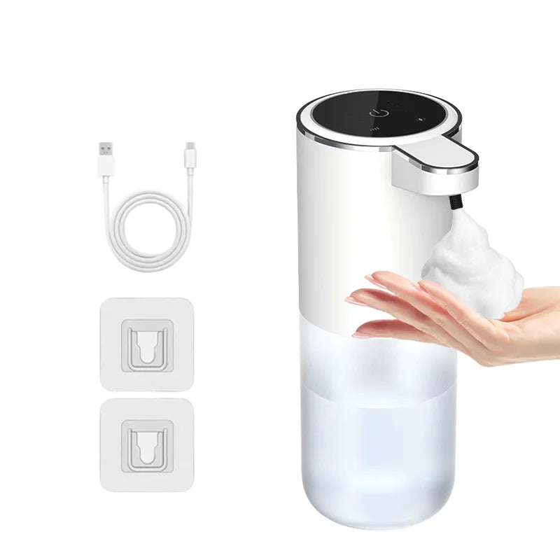A white touchless automatic soap dispenser with a pump head and a clear liquid reservoir is shown next to its charging cable 
