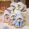 A fluffy white penguin plush toy wearing a hat sits next to other penguin toys on a white surface.