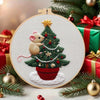 A circular embroidery kit featuring a handcrafted Christmas tree with a rabbit, set against a festive holiday background.
