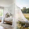 A bed canopy made of sheer white mosquito netting draped over a wooden bed in an outdoor setting.