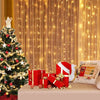 Christmas tree decorated with fairy lights and gifts in front of a warm golden curtain background