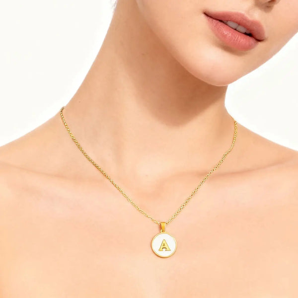 A gold-plated initial pendant necklace worn around the neck of a woman.