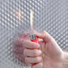 A hand holds a red foil liner with a flame on it against a gray geometric wallpaper background.
