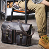 Dunkelbraunes Vintage-Ledertasche auf Holzboden neben einem Bein.