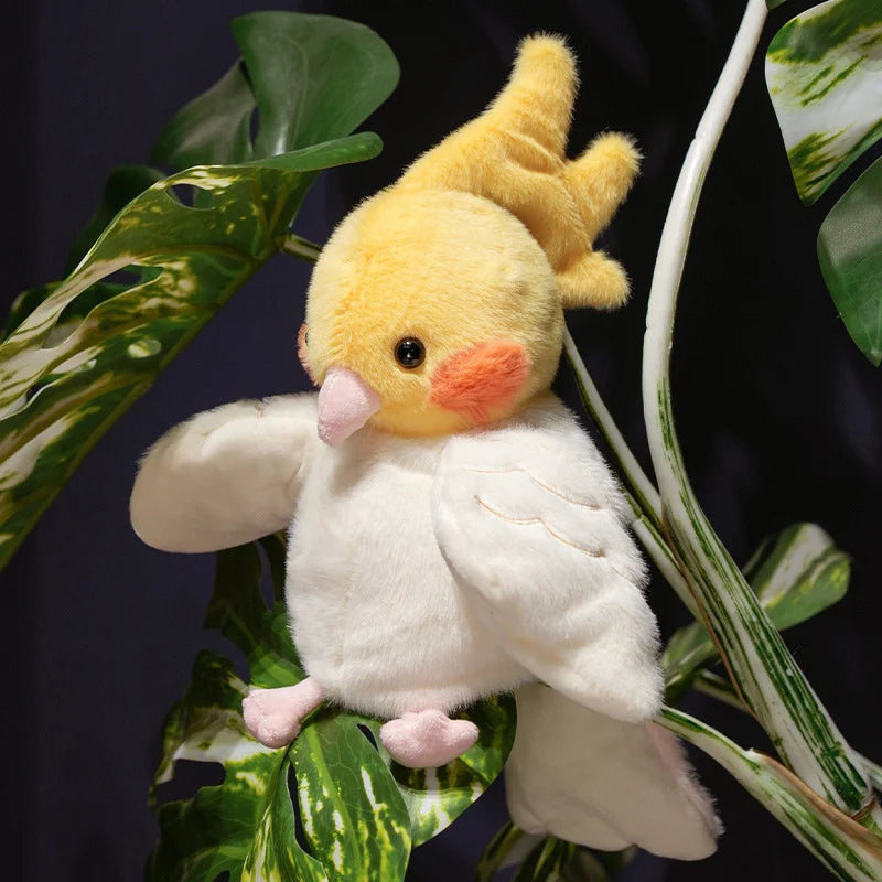 A fluffy yellow plush parrot hand puppet toy with pink feet perched on green leaves.
