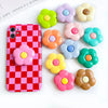 A pink checkered phone case is displayed next to several colorful, flower-shaped grips.