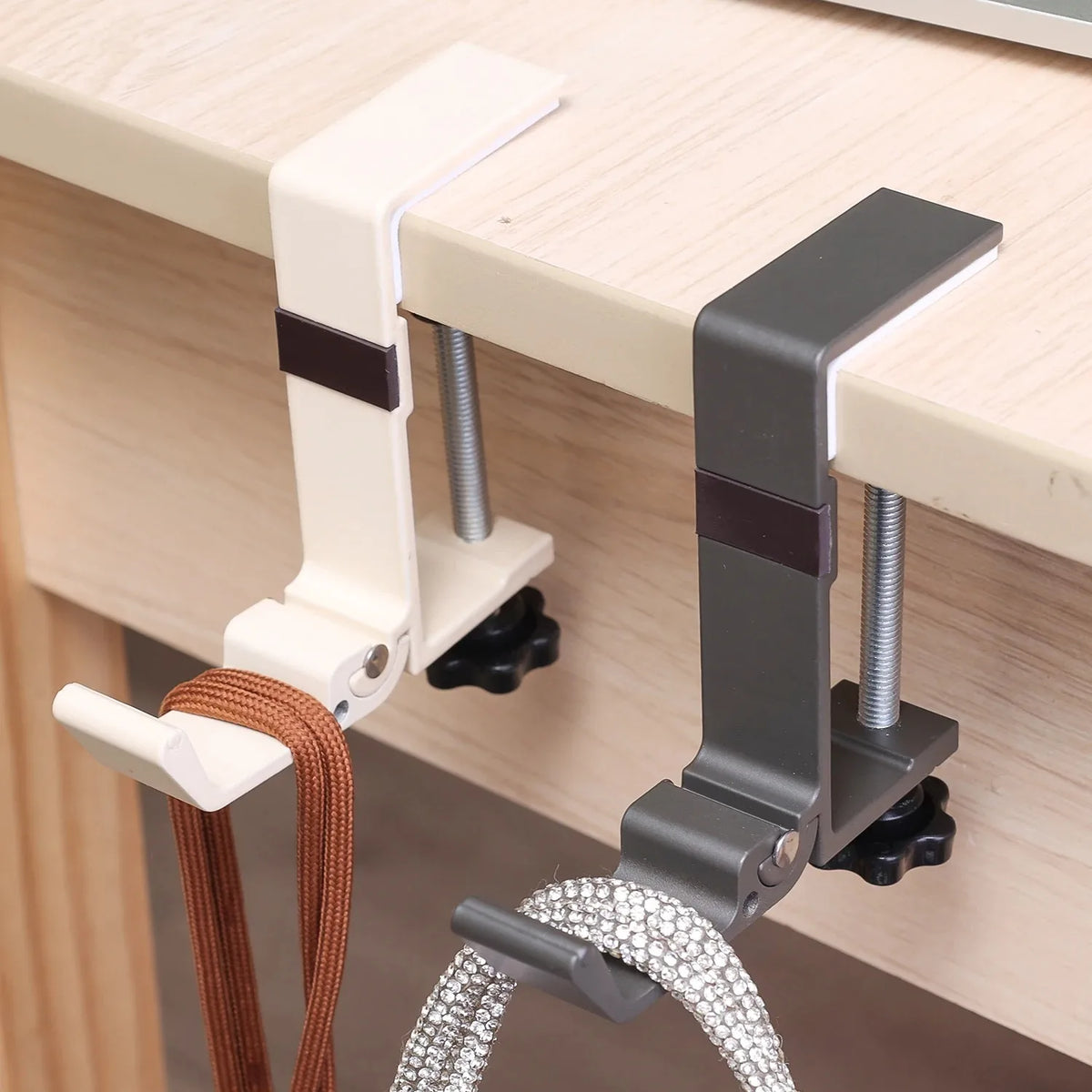 A close-up of a white and gray foldable aluminum desk hook designed for hanging bags and coats.