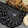 A black decorative rug shaped like a spider web with silver threads, placed next to a Halloween-themed fabric featuring bats 