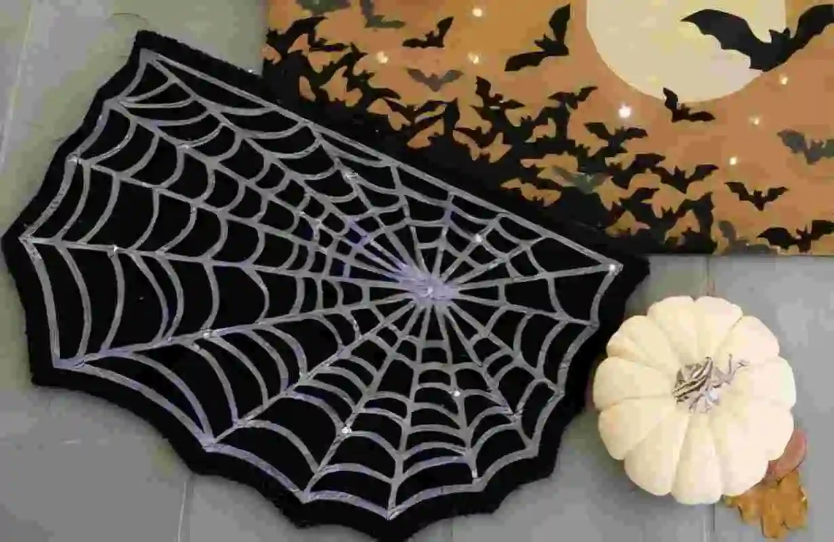 A black decorative rug shaped like a spider web with silver threads, placed next to a Halloween-themed fabric featuring bats 