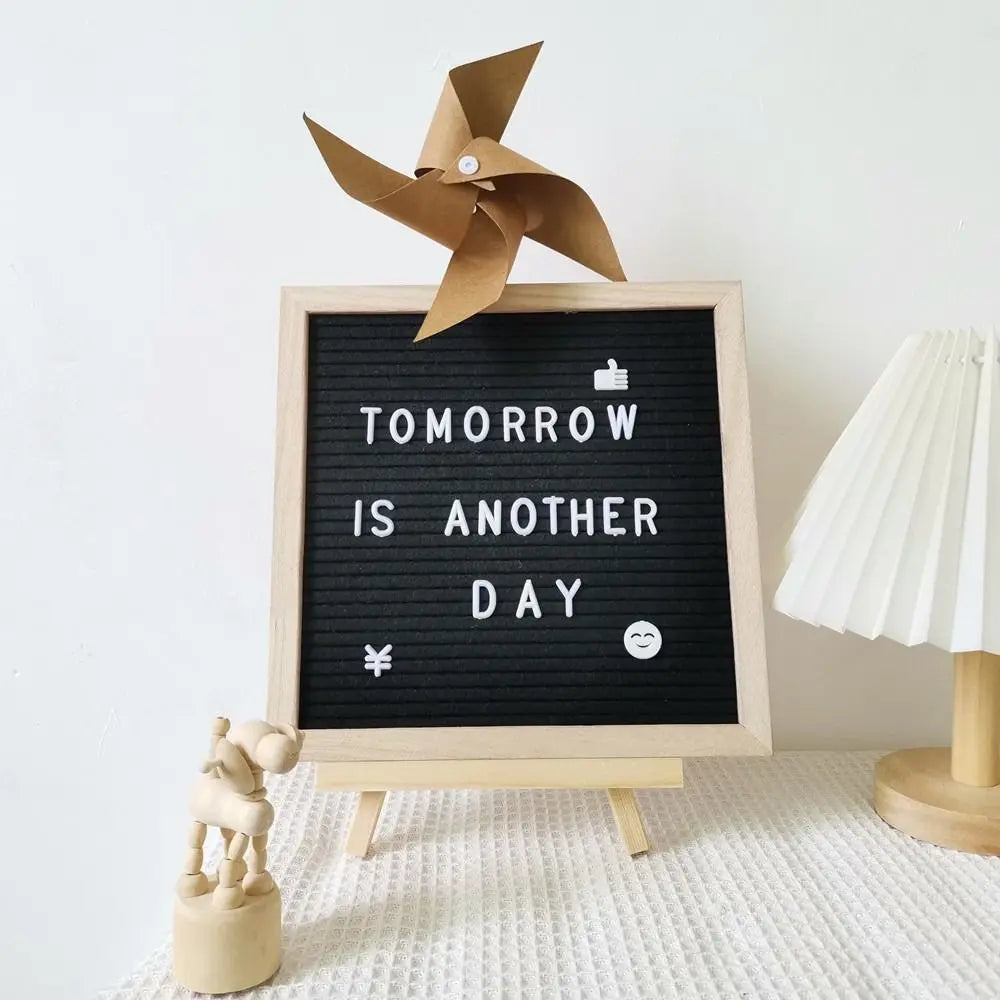 Tablero de fieltro negro con marco de madera que muestra el texto 'Tomorrow is another day' y un ventilador de madera.