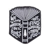 Black enamel pin featuring a stylized open book design with text inside