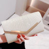 A hand holds a light beige pleated glitter envelope clutch with a gold chain strap.