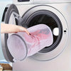 A hand places a reusable pink mesh laundry bag into the drum of a white washing machine.