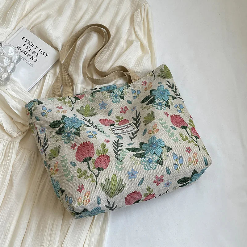A beige corduroy tote bag with floral accents resting on a white fabric background.