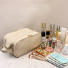 A beige waterproof PU leather cosmetic bag is shown next to various makeup and skincare products on a light surface.