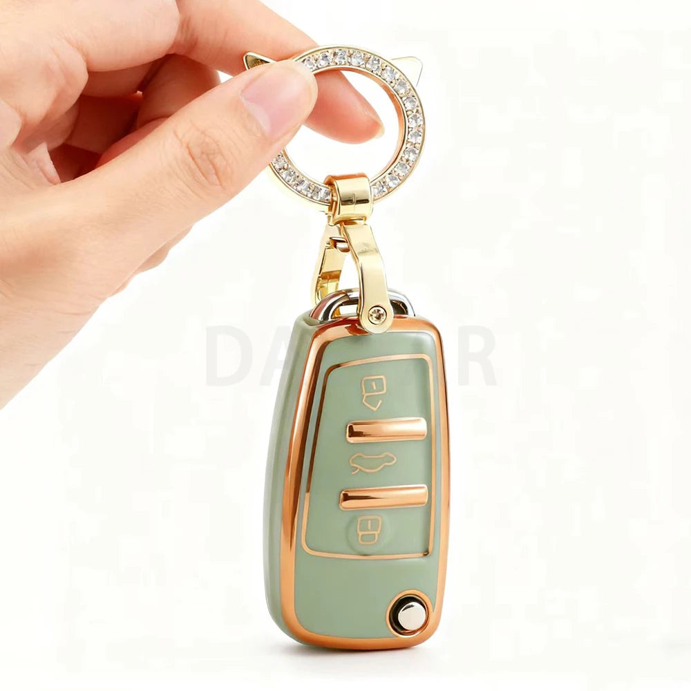 A close-up of a gold-toned key fob cover with a circular diamond charm and a protective TPU casing.