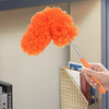 Orange extendable microfiber duster with a handle being used to clean dust from a corner.