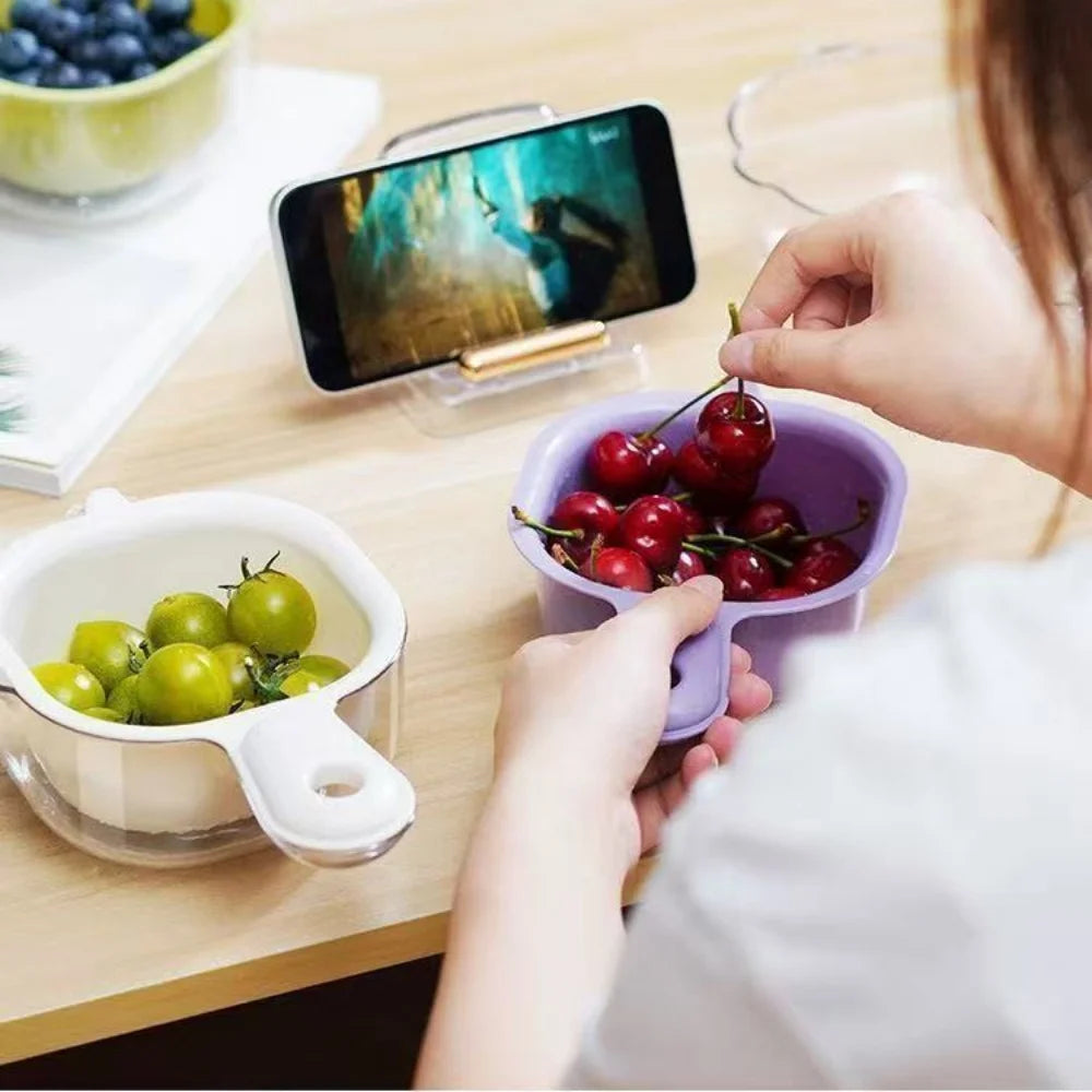A hand is holding a purple fruit washing basket filled with fresh cherries on a wooden table.