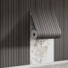 A close-up of wood grain peel-and-stick wall tiles installed on a gray wall, showing the texture and installation method.