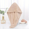 A beige microfiber towel wrap for hair is displayed on a white surface next to a potted plant.