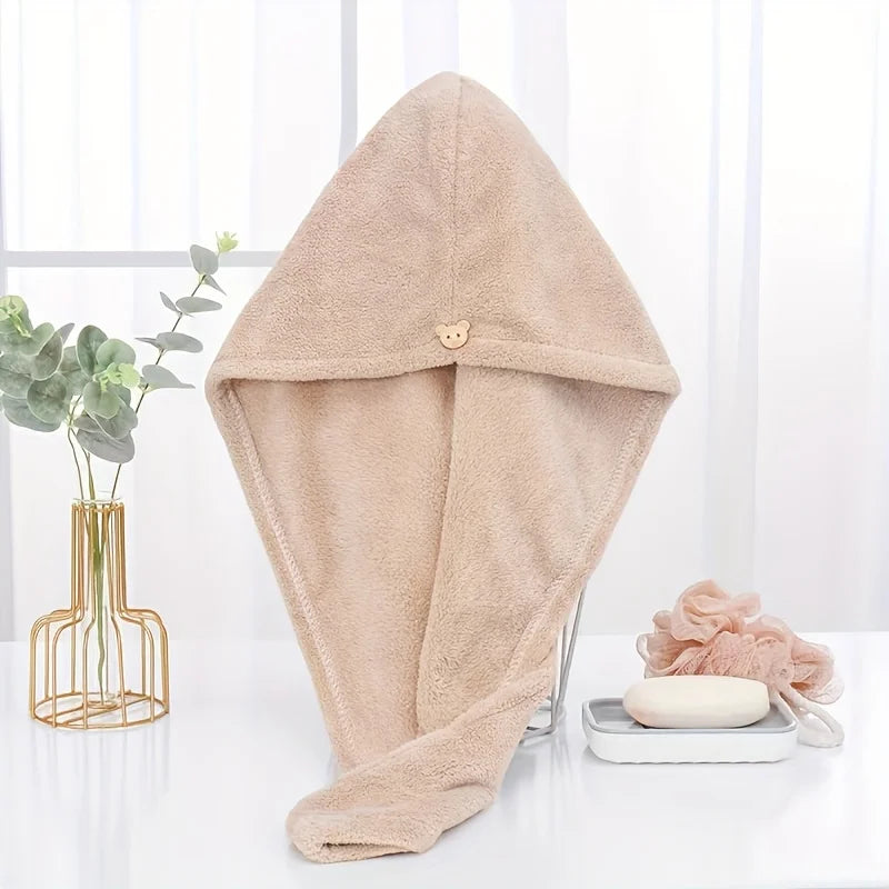 A beige microfiber towel wrap for hair is displayed on a white surface next to a potted plant.