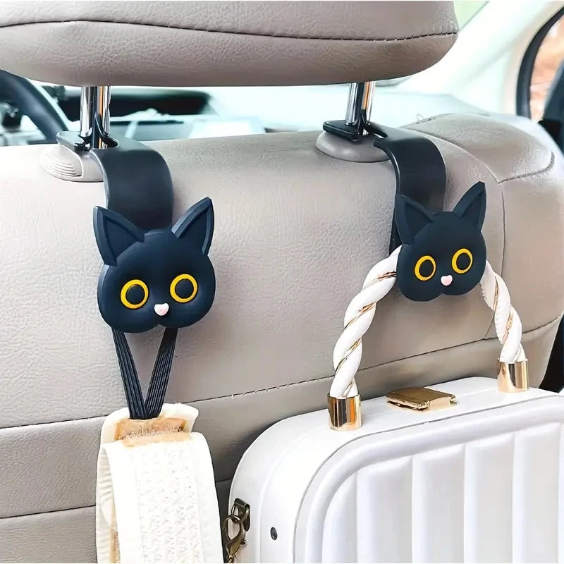 A set of two black cat headrest hooks with gold accents attached to a light gray car seat.