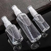 Three clear glass spray bottles with white pump tops are displayed on a dark surface.