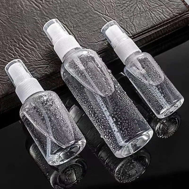 Three clear glass spray bottles with white pump tops are displayed on a dark surface.