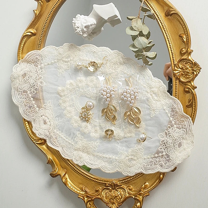 Elegant oval lace embroidered placemat with gold jewelry displayed in a gilded mirror frame.
