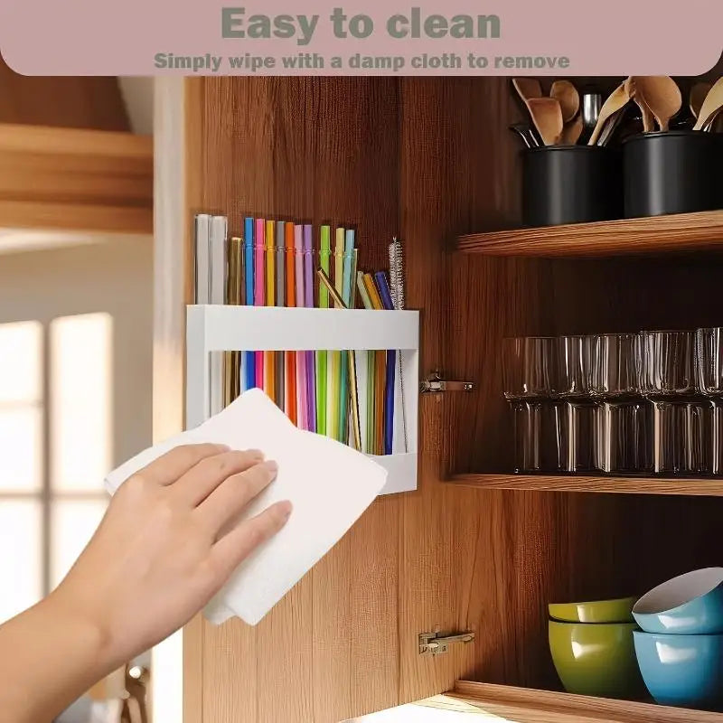 A hand wipes a white cloth on an acrylic straw dispenser mounted in a wooden cabinet shelf.