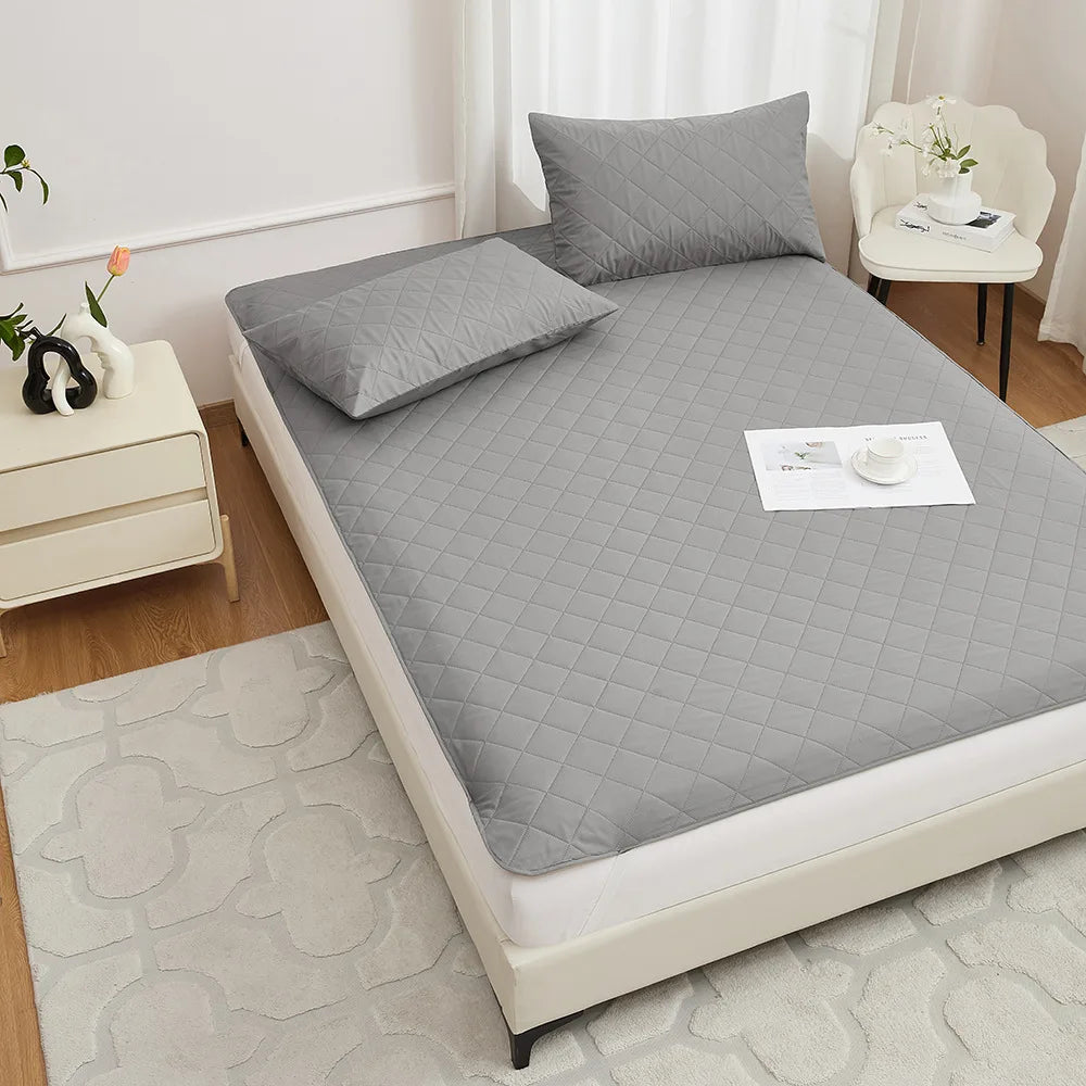 A gray waterproof mattress protector with elastic straps and a quilted pattern is displayed on a bed.