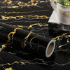 A roll of black marble self-adhesive wall sticker with gold veining lying on a dark surface.