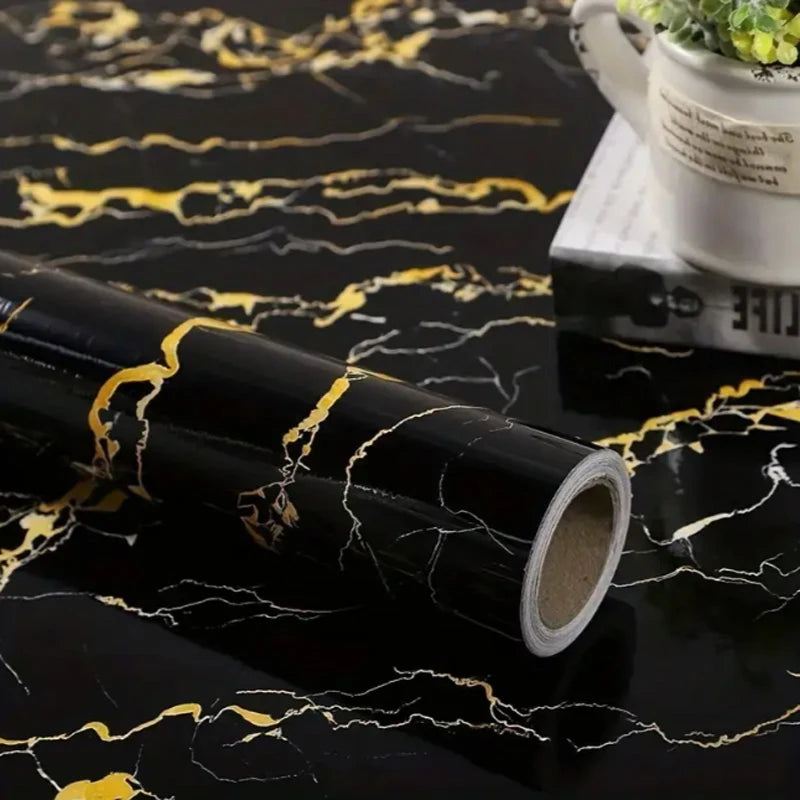 A roll of black marble self-adhesive wall sticker with gold veining lying on a dark surface.