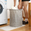 A gray checkered laundry basket with handles is placed on a mat next to a white washing machine.
