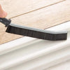 A black grout cleaning brush with a gray handle is shown resting on a white window frame.