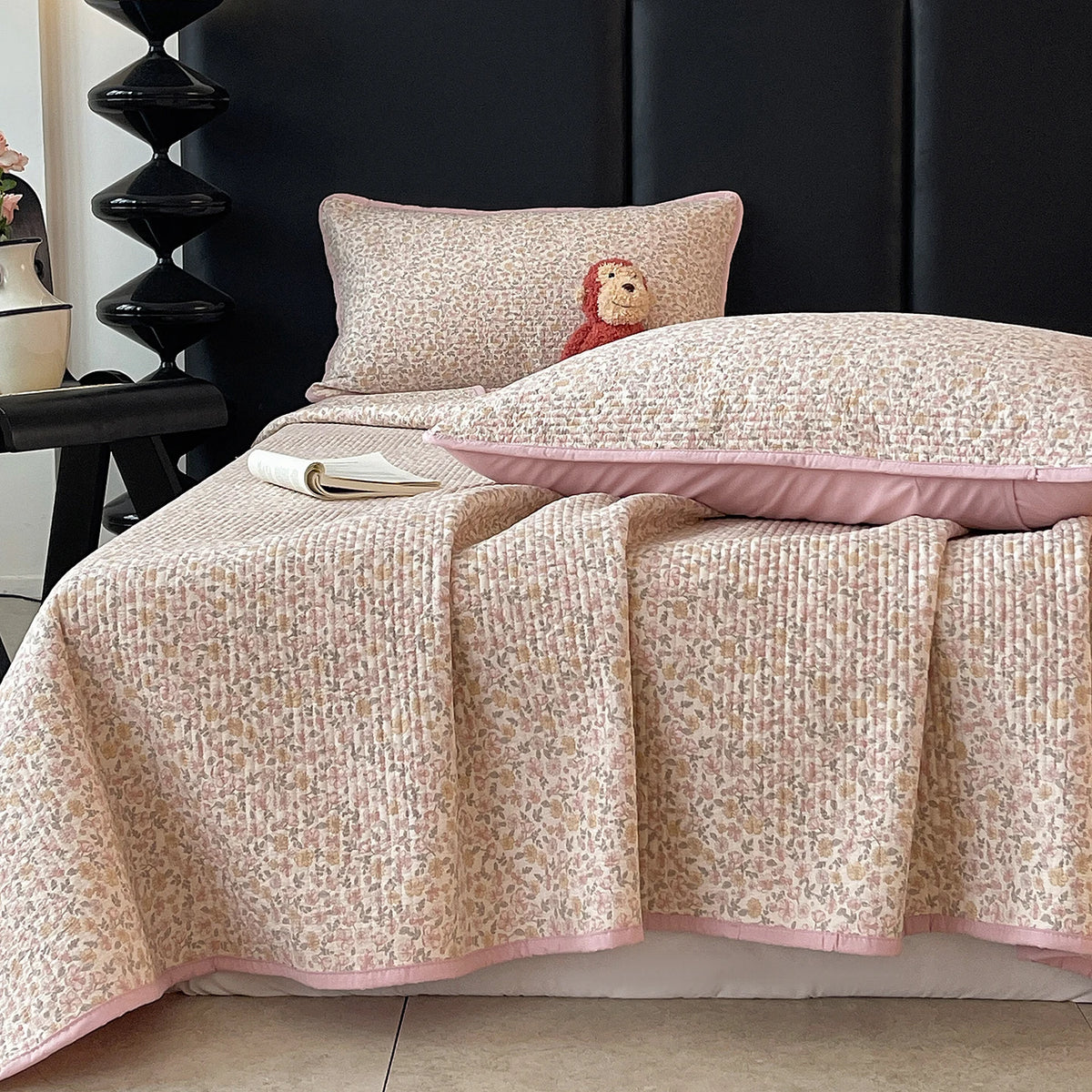 A floral quilted bedspread in soft beige and pink tones is draped over a dark headboard.