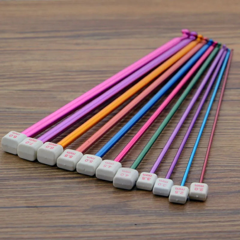 A set of 23 colorful Tunisian crochet hooks with bamboo cables arranged diagonally on a wooden surface.