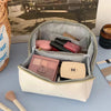 A light pink cosmetic storage bag with a lid is open, revealing various makeup products and tools.