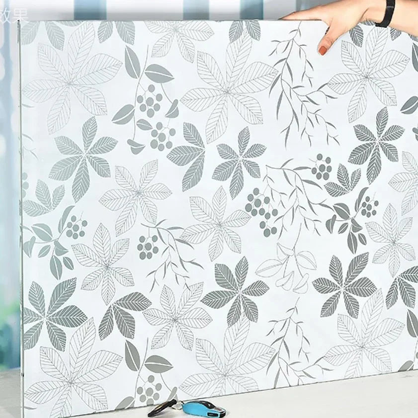 A roll of frosted privacy window film with a gray leaf and berry pattern is shown against a white background.
