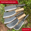 A set of hand-forged steel wood cutters with wooden handles resting on a stone and greenery.