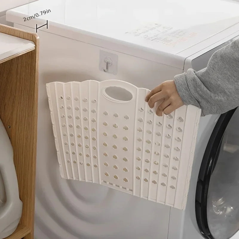 A white folding laundry basket with handles is shown hanging on the door of a washing machine.