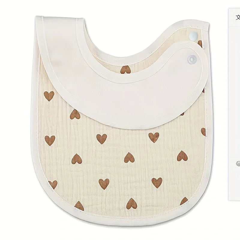 A light beige baby cotton gauze bib with a curved top and a scalloped edge, featuring small brown heart embroidery.
