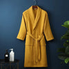 A mustard yellow lightweight cotton waffle robe hanging on a dark blue wall.