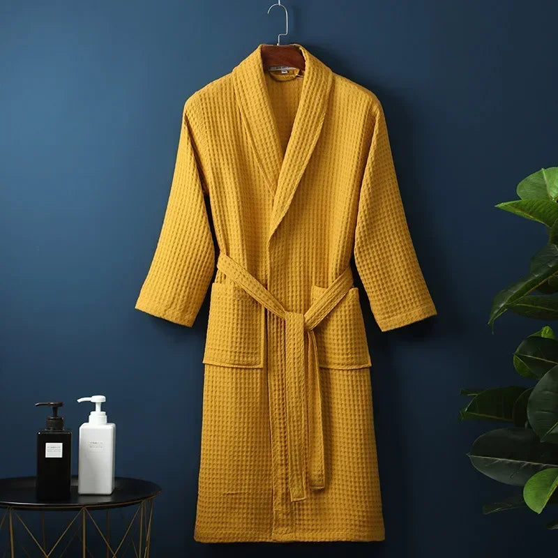 A mustard yellow lightweight cotton waffle robe hanging on a dark blue wall.