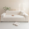 A cream colored plush sofa cover with a light wood tray and greenery on a white rug.