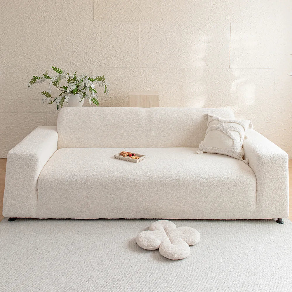 A cream colored plush sofa cover with a light wood tray and greenery on a white rug.