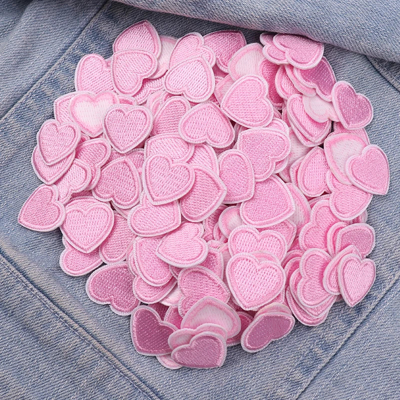 A pile of pink heart-shaped embroidered patches for DIY clothing decoration on a denim fabric.