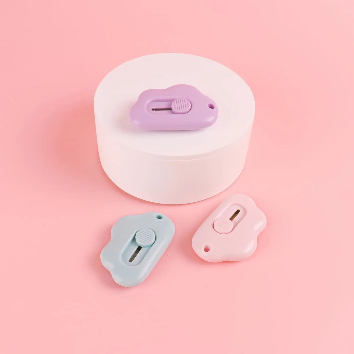A light purple cloud-shaped retractable letter opener with a keychain loop resting on a white circular base.